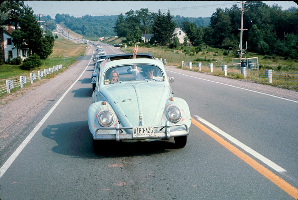 A man driving a Volkswagen Beetle makes his way to the Woodstock Music and Arts Fair as he flashes a peace sign through the sunroof in 1969.