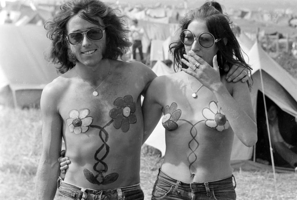 A couple with matching flower body paint walks together during the Isle of Wight Festival in the UK in 1970.